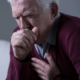 An image of a senior man suffering from constant throat clearing coughing intohis fist.
