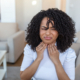 An image of a woman with post nasal drip holding her throat in discomfort.