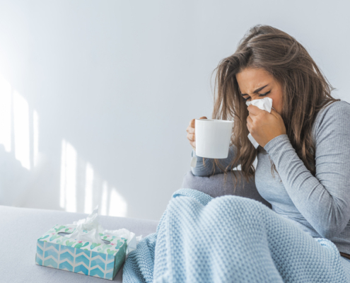 An image of a woman with nasal congestion sitting on a couch wiping her nose with a tissue.