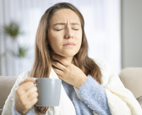 An image of a woman with recurring throat infections holding her throat in pain.