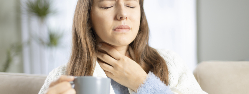 An image of a woman with recurring throat infections holding her throat in pain.