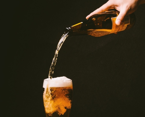 An image of a hand pouring beer into a glass to limit alcohol intake.