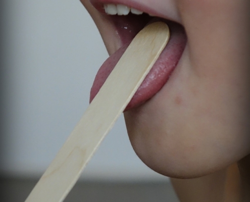 An image of a tongue depressor in child's mouth for a throat exam.