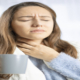 An image of a woman holding her sore throat.