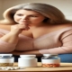 Qsymia vs Phentermine: An attractive overweight woman in her mid-50s sitting in a brightly lit living room, thoughtfully contemplating two types of weight loss pills on a small coffee table.